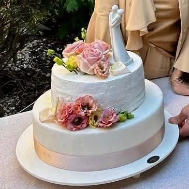 Torta nuziale bianca con rose rosa e statuine degli sposi, servita in giardino