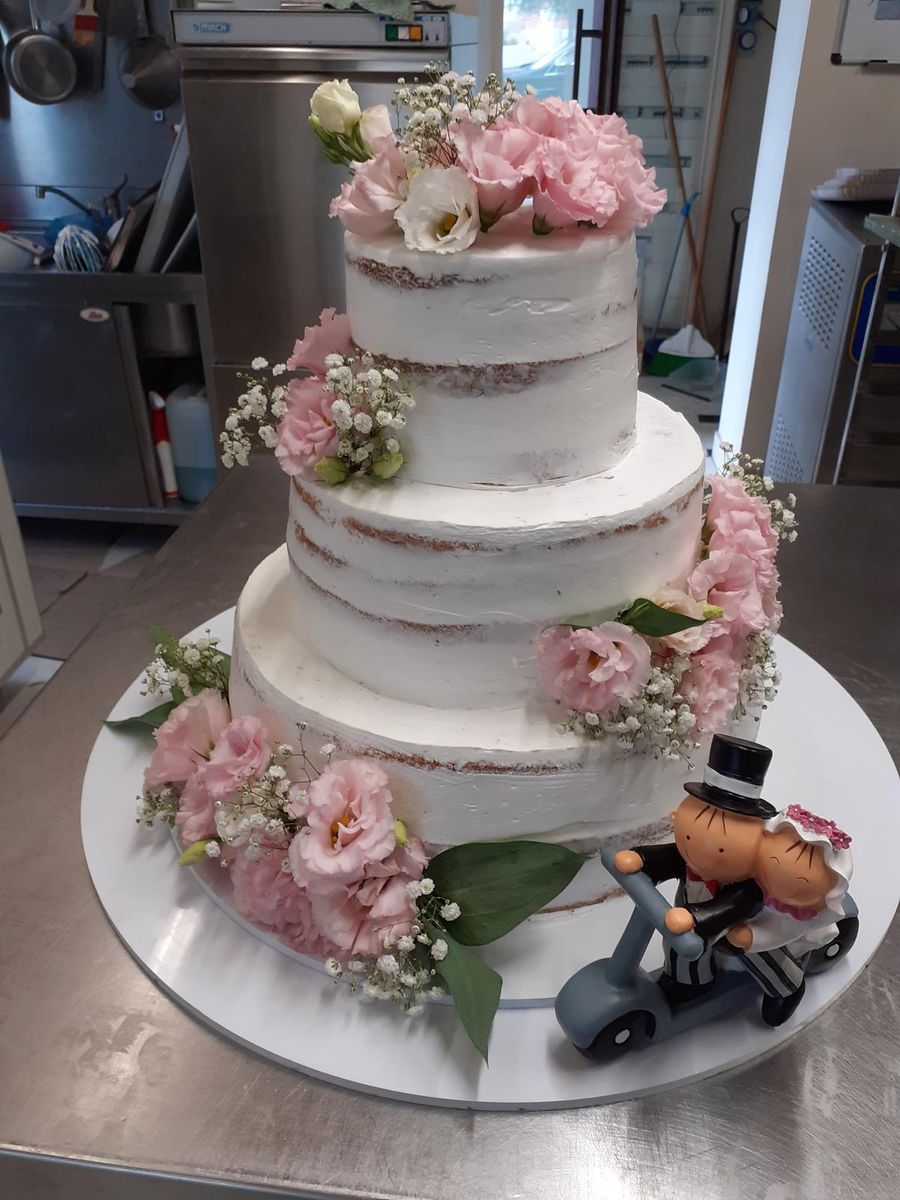 Torta nuziale a piani con fiori rosa e statuine degli sposi in moto
