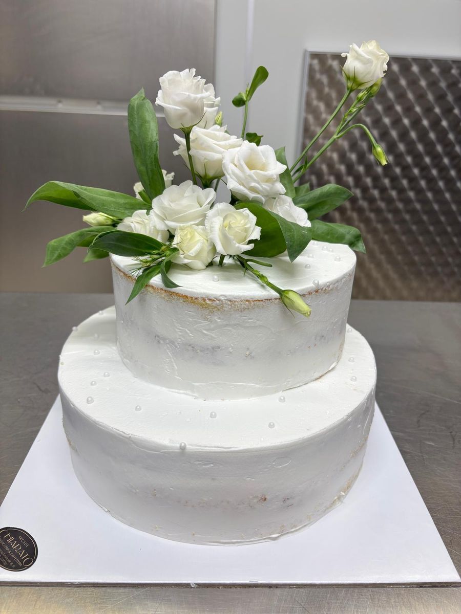 Torta nuziale a due piani semi-nuda con rose bianche e foglie verdi